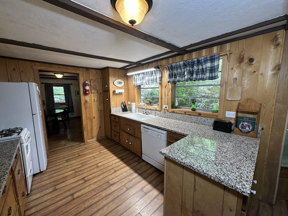 Granite countertops stretch along wood-paneled walls beneath two windows with blue plaid valances.