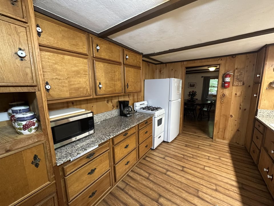 Wood-paneled kitchen with granite countertops, white gas stove, refrigerator, and built-in microwave.