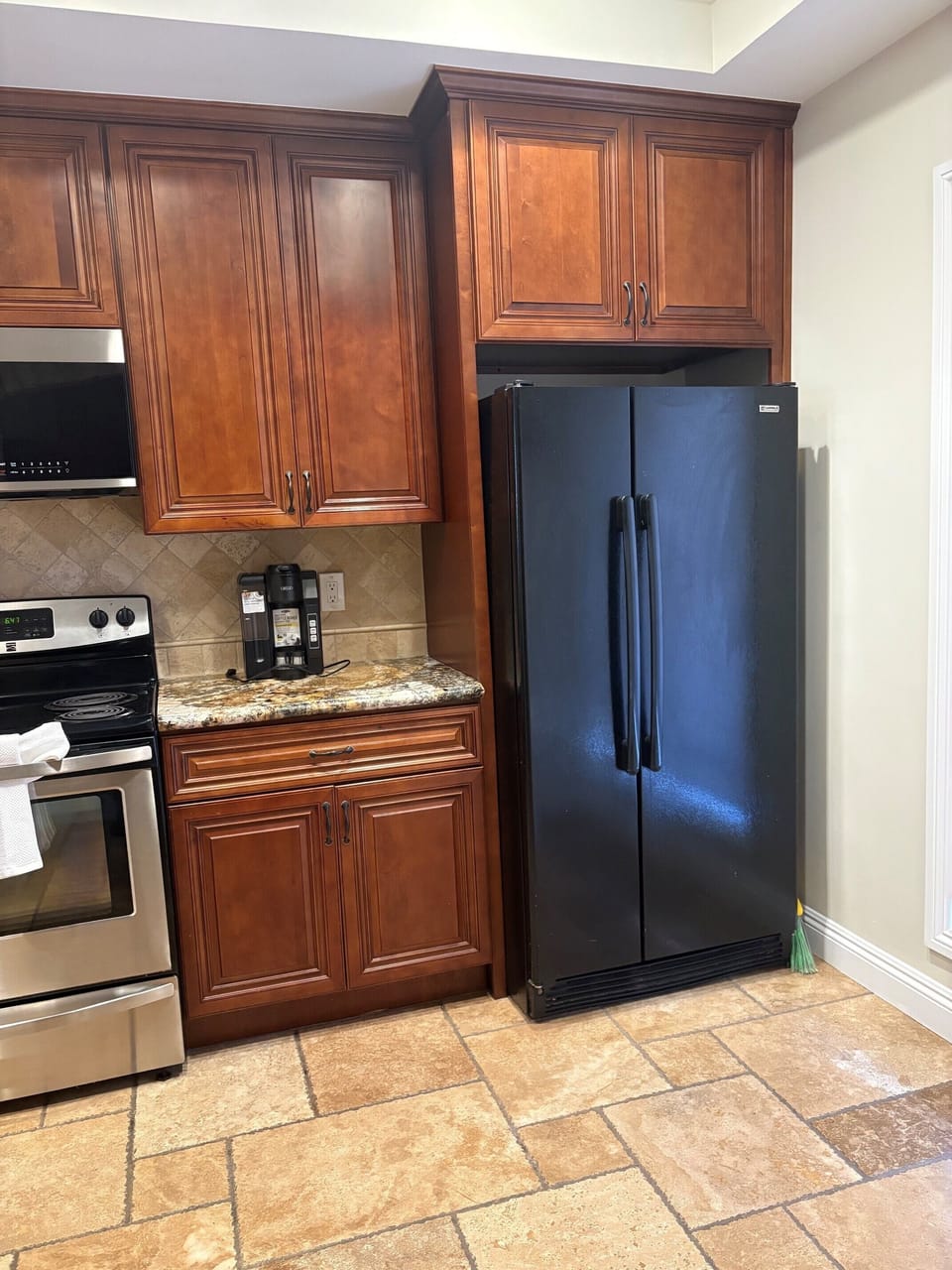 Your well-appointed kitchen features rich wood cabinetry, granite counters, and full-sized stainless appliances, including a refrigerator, oven, and even a coffee maker ready for your morning brew.