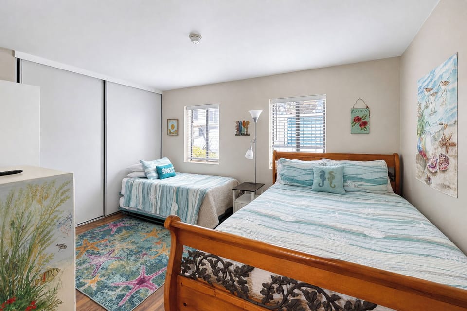 Your private seaside retreat features two cozy beds dressed in calming coastal linens, framed by cheerful beach-themed artwork that sets the perfect tone for your getaway.