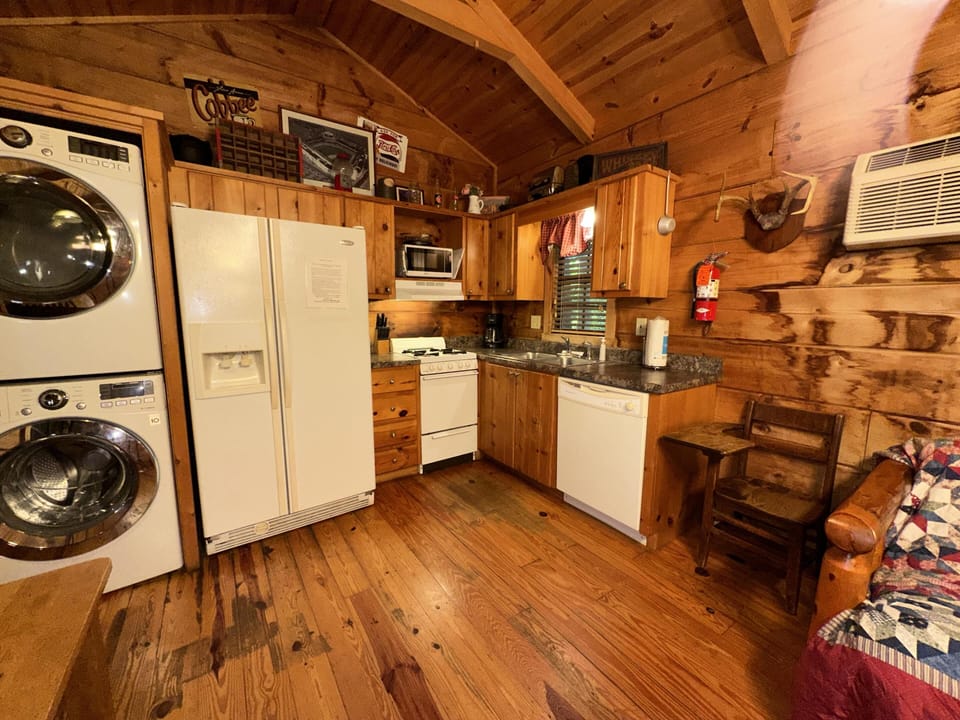 Stacked washer and dryer sit beside white appliances and knotty pine cabinets in the compact kitchen area.
