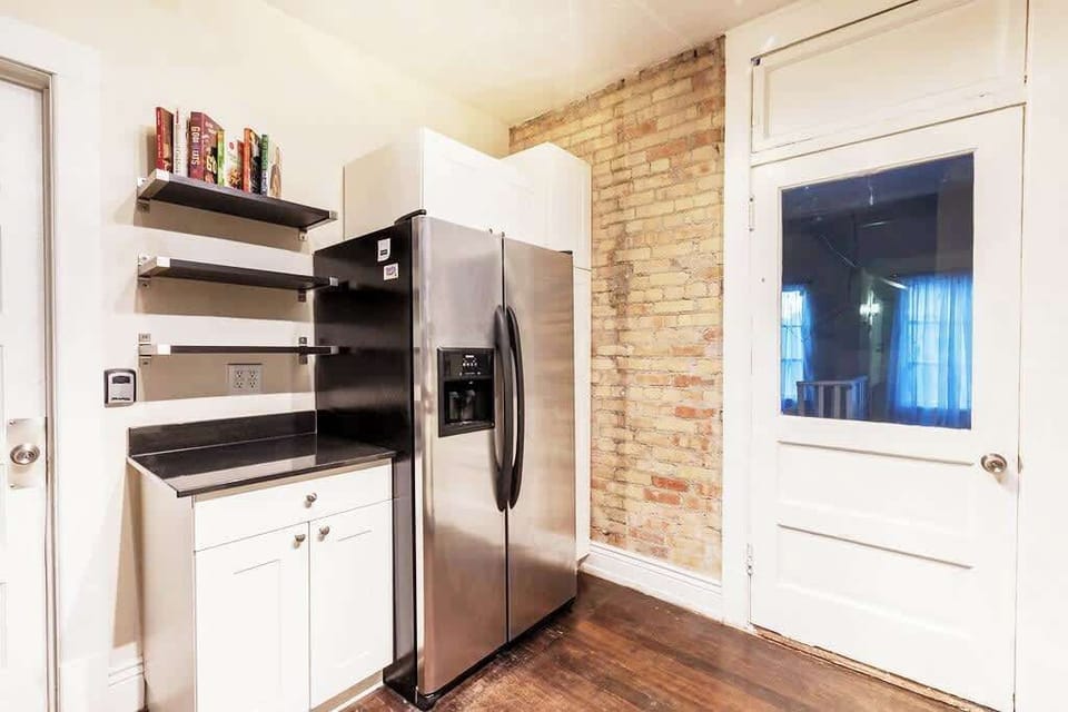 Kitchen corner with stainless steel fridge, open shelving, and charming brick accents for added character.