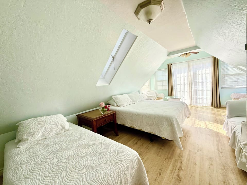 Drift off in the serene attic bedroom, where two plush beds, soft natural light from skylights, and peaceful mint walls create your perfect restful retreat.