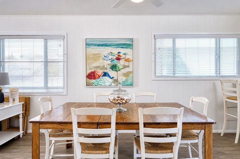 Step into your bright, beach-inspired dining space where coastal charm meets comfort. Gather around the farmhouse table under natural light, with cheerful artwork setting a relaxed, seaside mood for meals together.