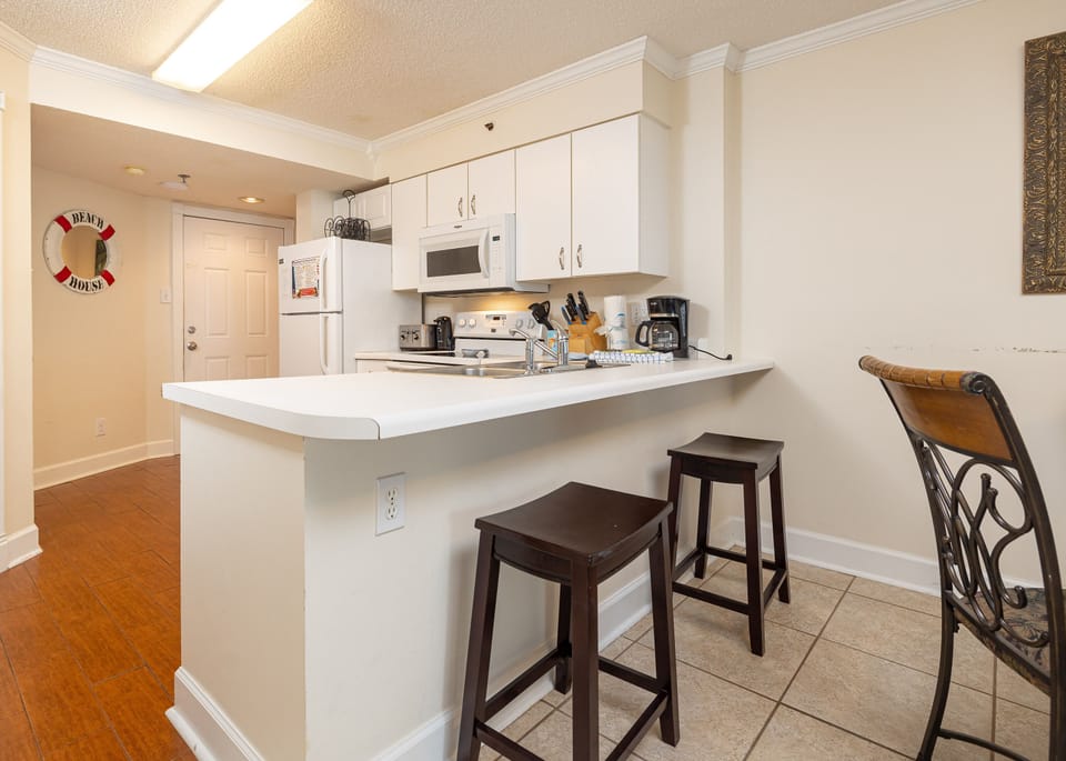 This kitchen features white cabinetry, essential appliances, and a breakfast bar with seating, perfect for casual dining
