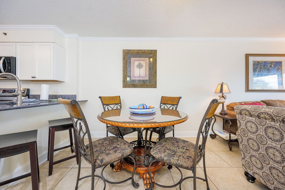 The living area features a round dining table, plush seating, and a stunning beachfront view through large sliding doors