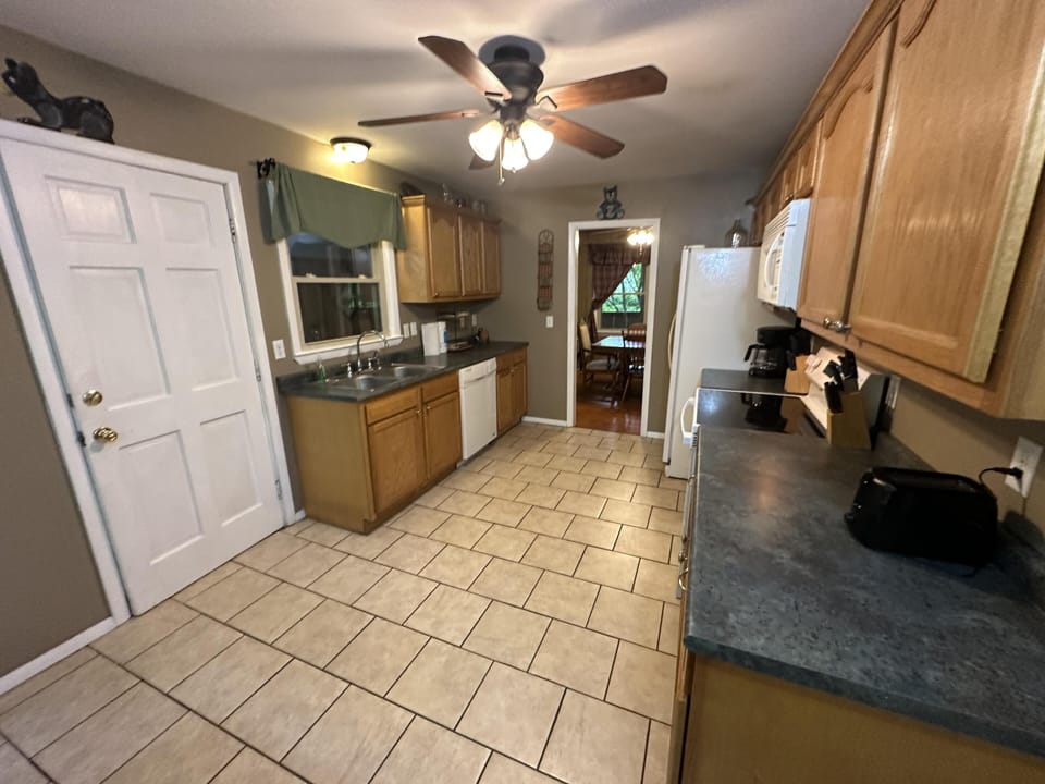 Galley kitchen with tile flooring, oak cabinets, dark gray countertops, and ceiling fan lighting.