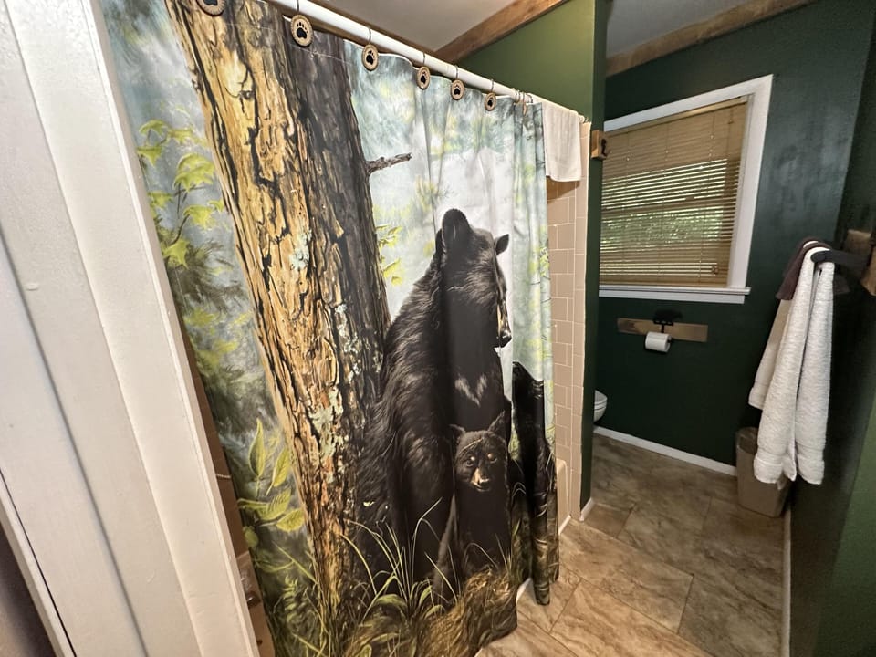Bathroom with dark green walls, tiled floor, and a shower curtain featuring a bear family design.