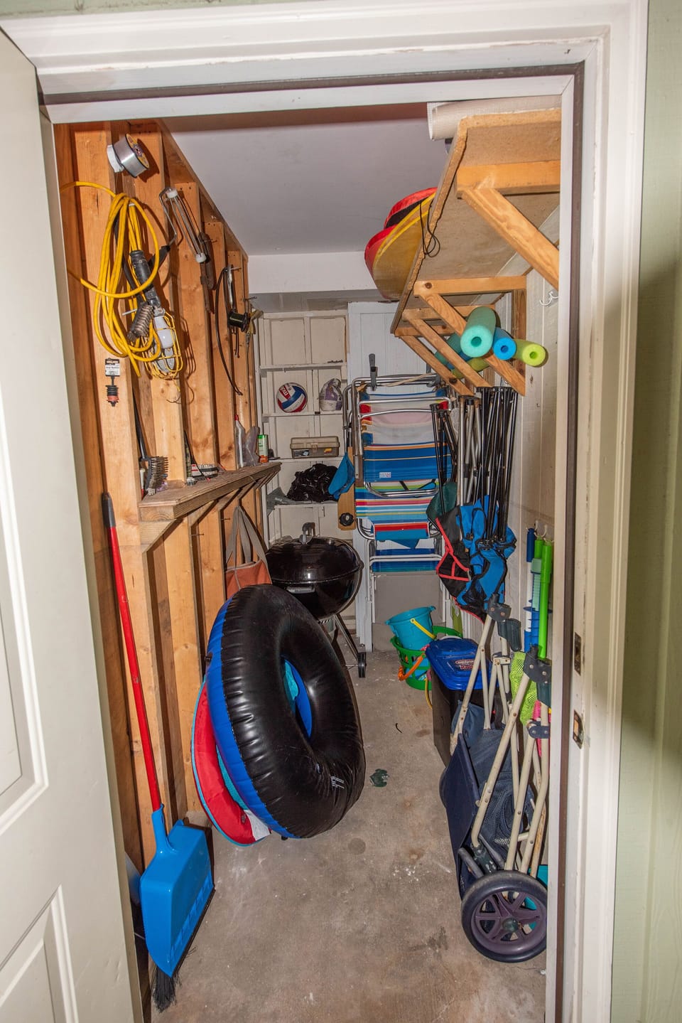 Storage room contains beach chairs, beach umbrella, beach toys and grill.