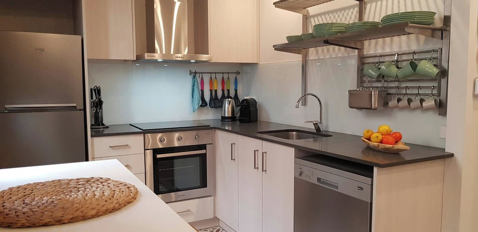 The modern kitchen is equipped with stainless steel appliances including a dishwasher, oven, and stovetop, making it easy to prepare meals during your stay. The kitchen features a sleek, minimalist design and is well-lit, creating an inviting space to enj