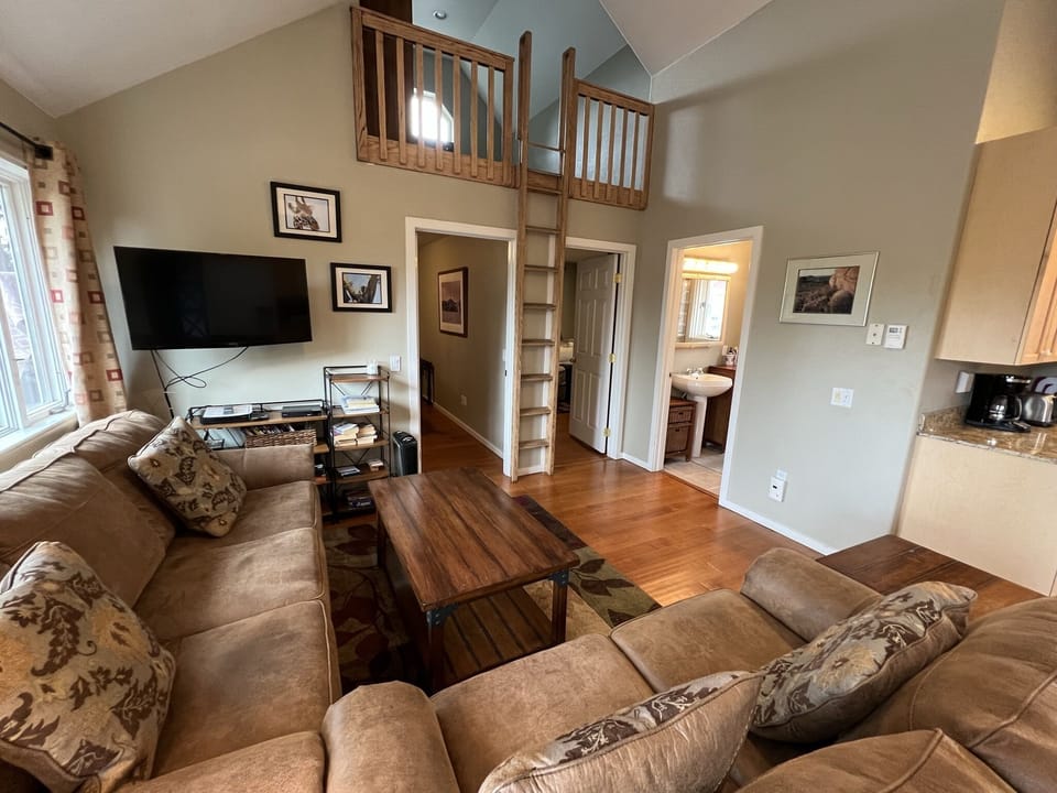 Living room with vaulted ceiling and open floor plan, HD TV, door to deck.