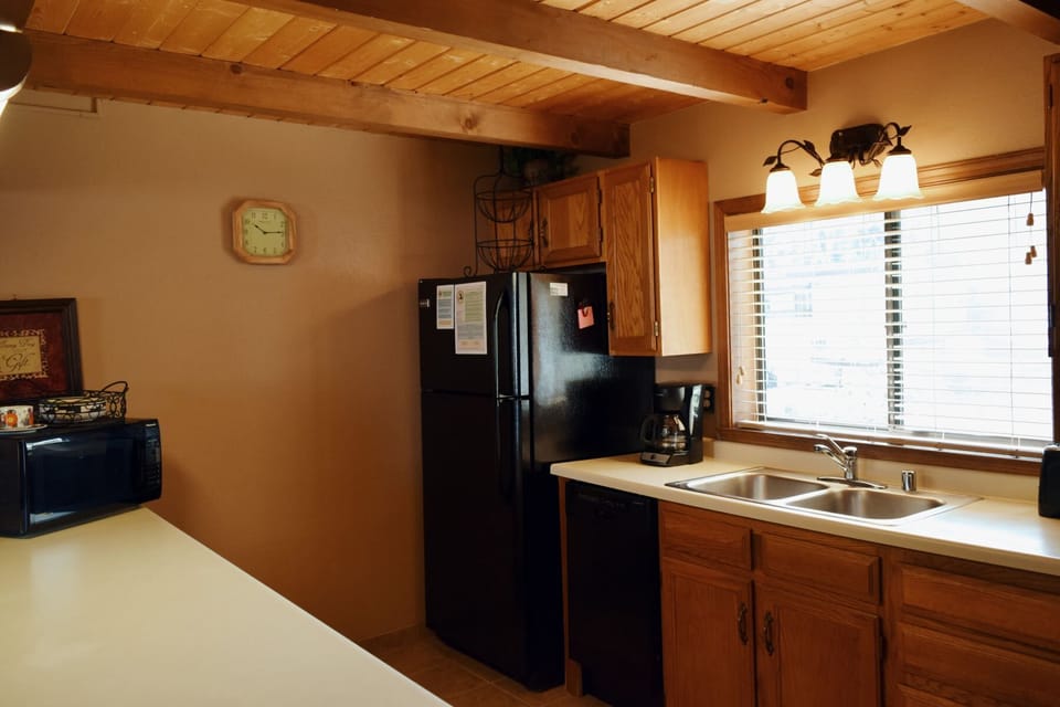 Step into your fully equipped kitchen with exposed beam ceilings, where you'll find everything needed to prepare meals—from the spacious refrigerator and microwave to the bright natural light streaming in.