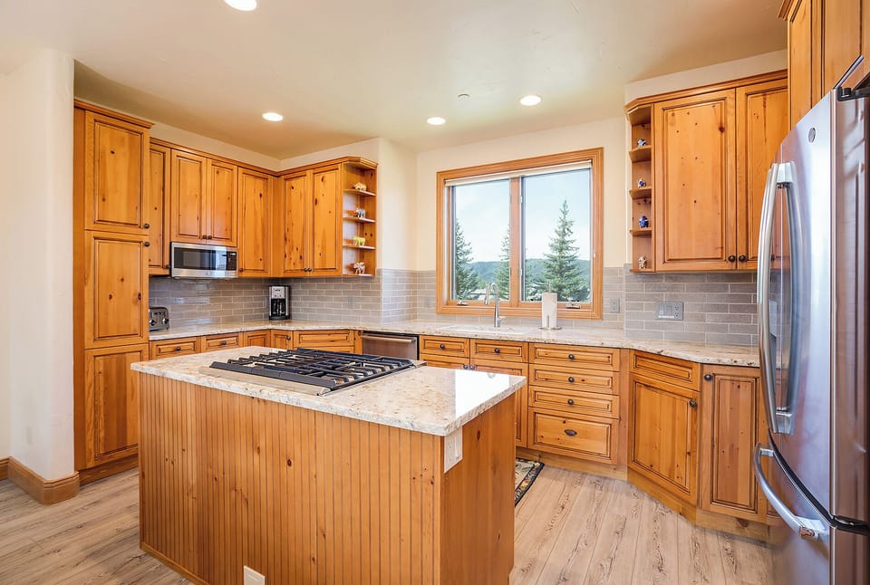 Your spacious kitchen features warm wood cabinets, granite countertops, and modern appliances with mountain views from the window.