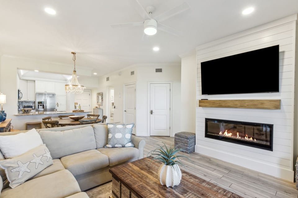 Living Area with a Tan Sectional Positioned around a Large Flat Screen Smart TV and Electric Fireplace