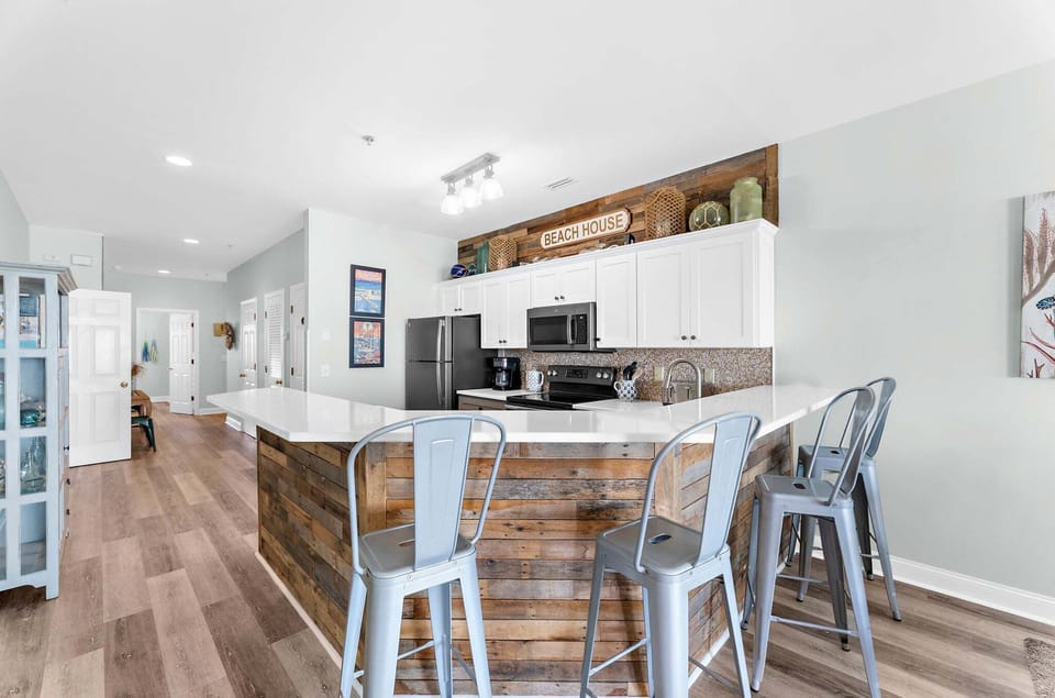 Open concept kitchen with sleek finishes and convenient bar seating for three, perfect for casual dining or entertaining after a day at the beach.