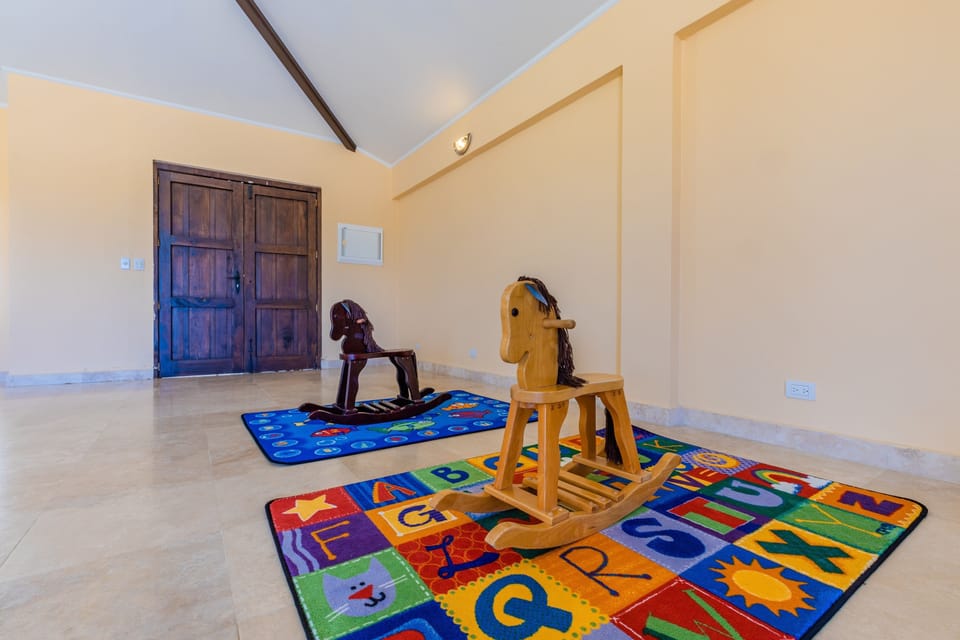 Your little ones can explore and play freely in this spacious, safe indoor playroom featuring colorful learning mats and charming wooden rocking horses.