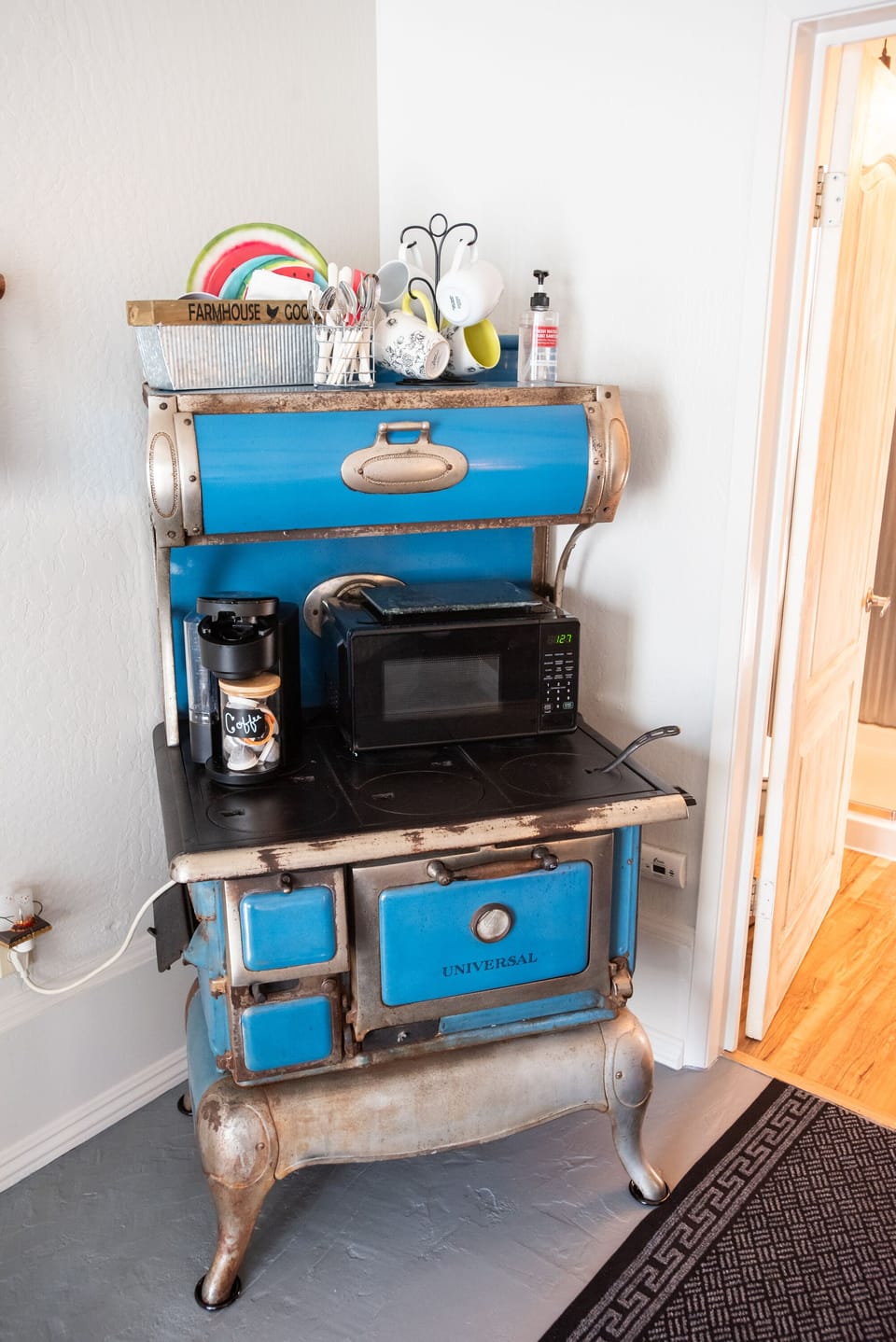 Vintage stove repurposed as a coffee bar with microwave and dishware.
