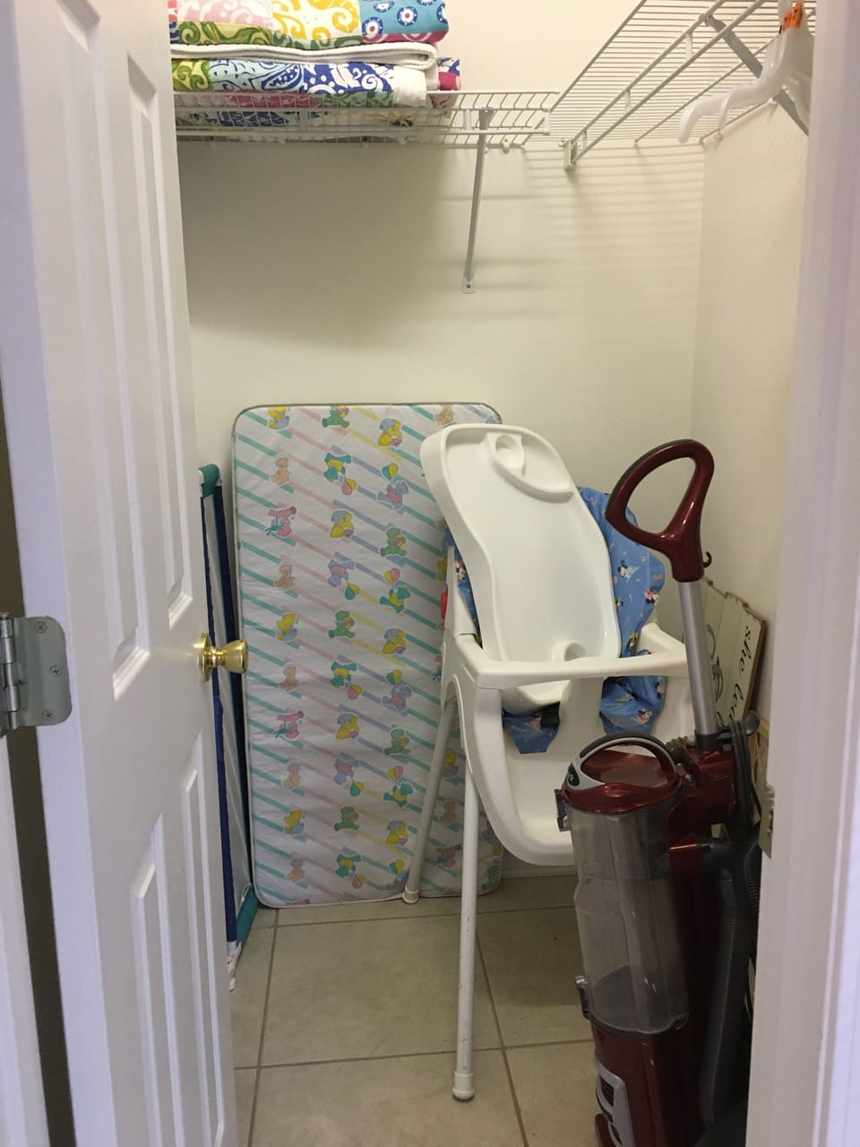 The room has a walk in closet with a highchair, baby gate, and bed rail.