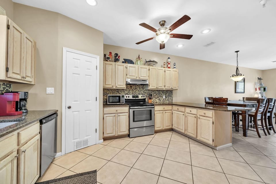 Tile floors extend through the kitchen with light wood cabinets, mosaic backsplash, and stainless appliances.