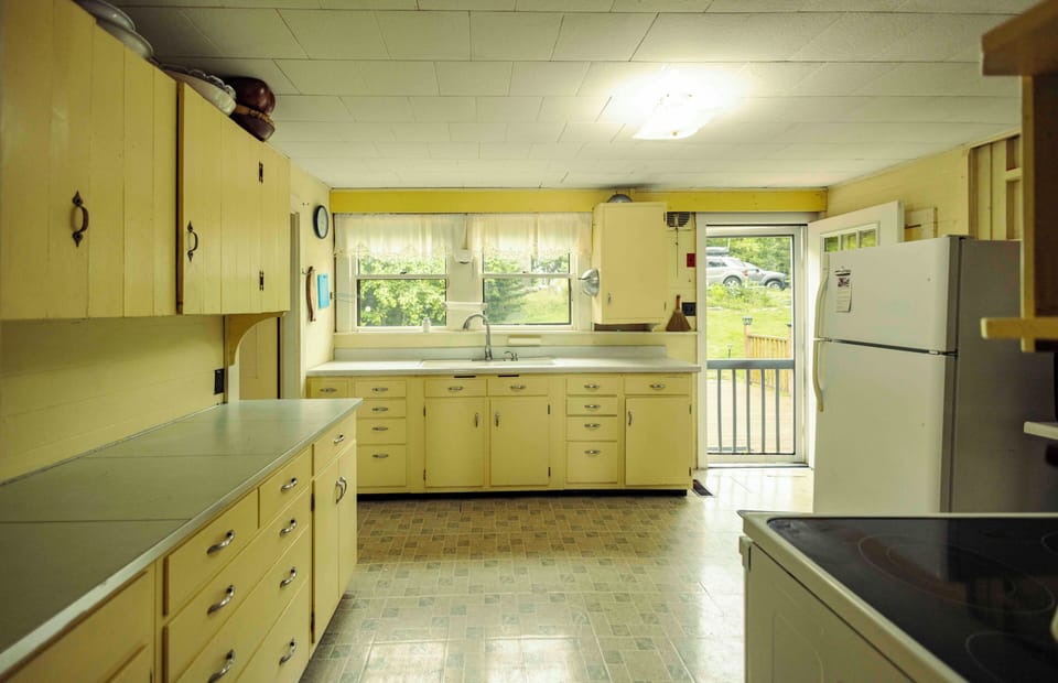 Kitchen with view to the sunny front porch, lawn, garden, and woods.