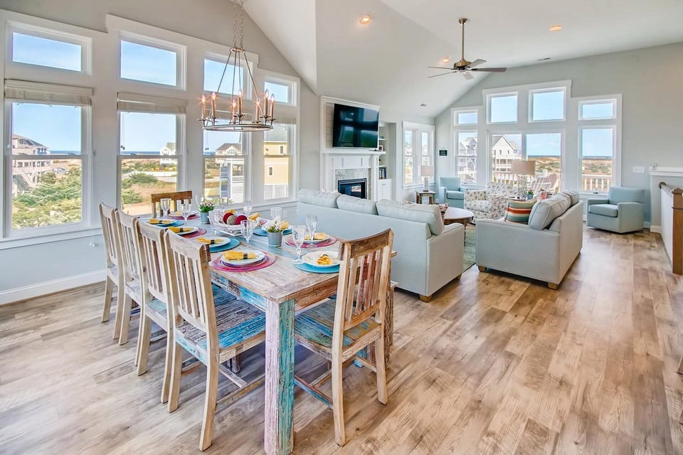 Gather around the dining table or sink into the plush seating, where expansive windows frame sweeping coastal views and vaulted ceilings create an airy, light-filled retreat perfect for relaxing.
