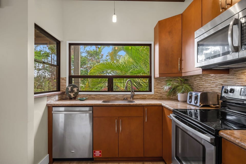 Prepare meals in a bright kitchen featuring stainless steel appliances, rich wood cabinetry, and a large window framing tropical views.