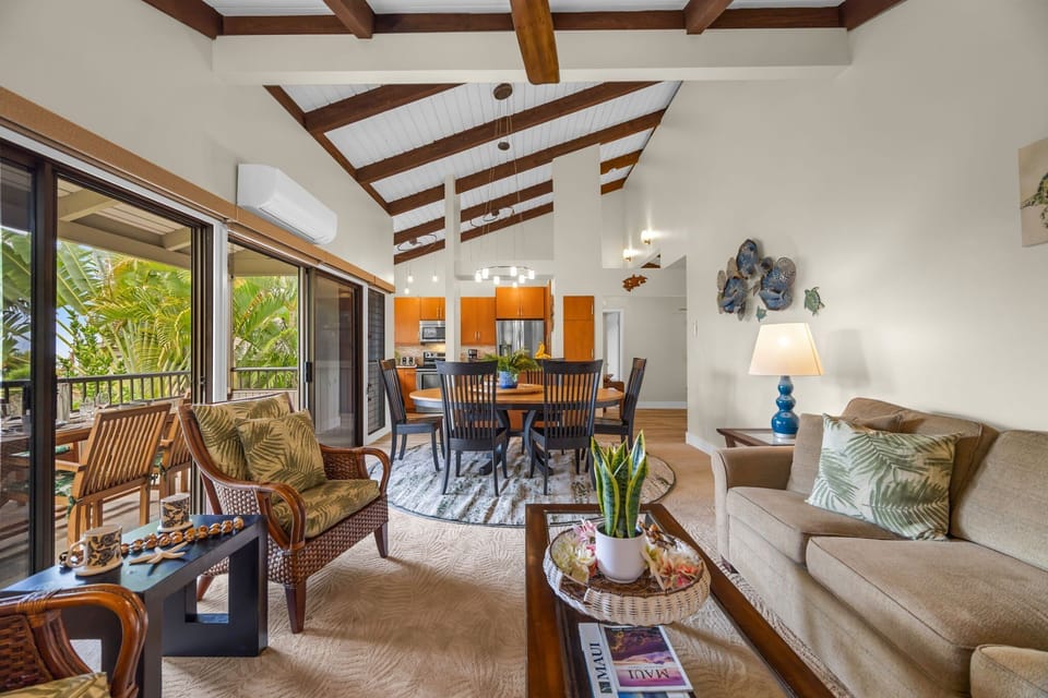 Step into a spacious living and dining area featuring vaulted ceilings with exposed beams, cozy seating, and large sliding doors that open to the lanai.