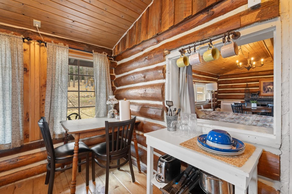 Small dining nook with two black chairs, a wooden table, and sheer curtains overlooking the yard.