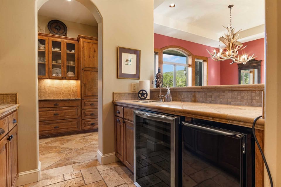 The functional butler's pantry and wet bar feature rich wood cabinetry, integrated wine cooling, and tiled countertops, offering a convenient service hub between the kitchen and the elegant dining room.