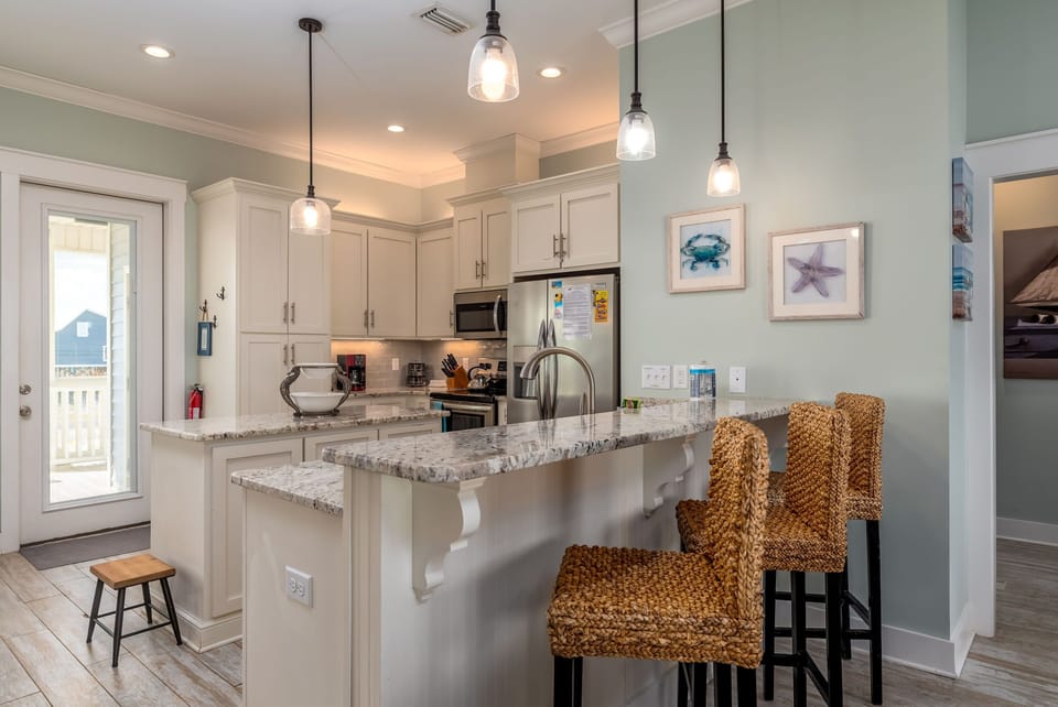 Your coastal-inspired kitchen awaits with granite counters, pendant lighting, and wicker bar stools perfect for morning coffee or evening appetizers.