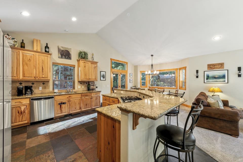 Your open-concept kitchen flows into the living area, featuring granite counters, warm wood cabinets, and mountain views through every window.