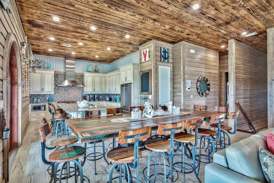 Open dining area w/ long table, bar seating, and rustic beams ideal for group meals