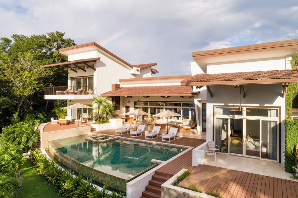The stunning Villa Belvedere, with a spacious balcony, an inviting outdoor dining area, and a picturesque backyard featuring a swimming pool
