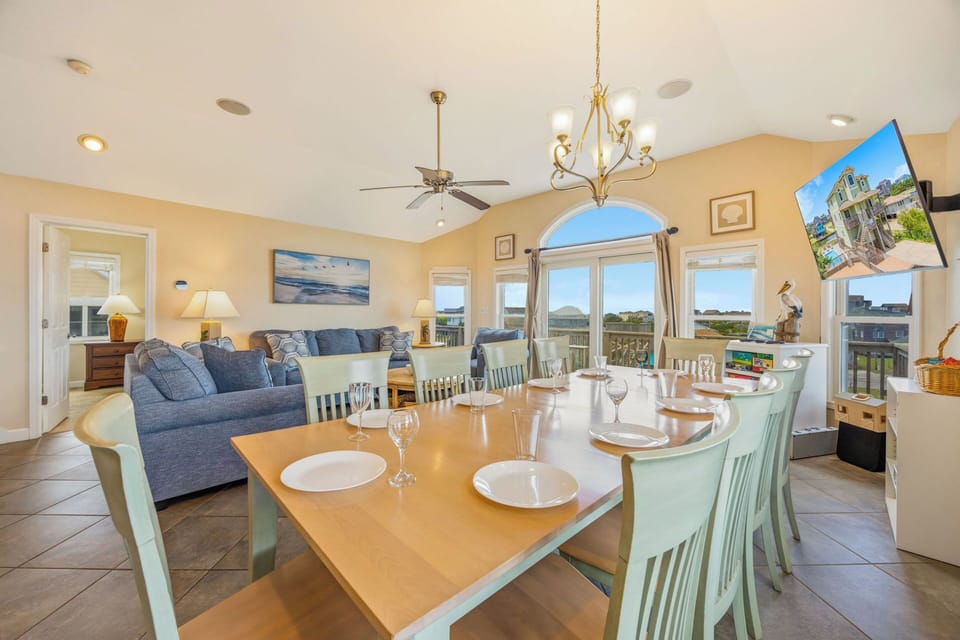 Gather around the spacious dining table for memorable meals together, surrounded by coastal décor and flooded with natural light from the arched windows that frame peaceful views of the surrounding landscape.