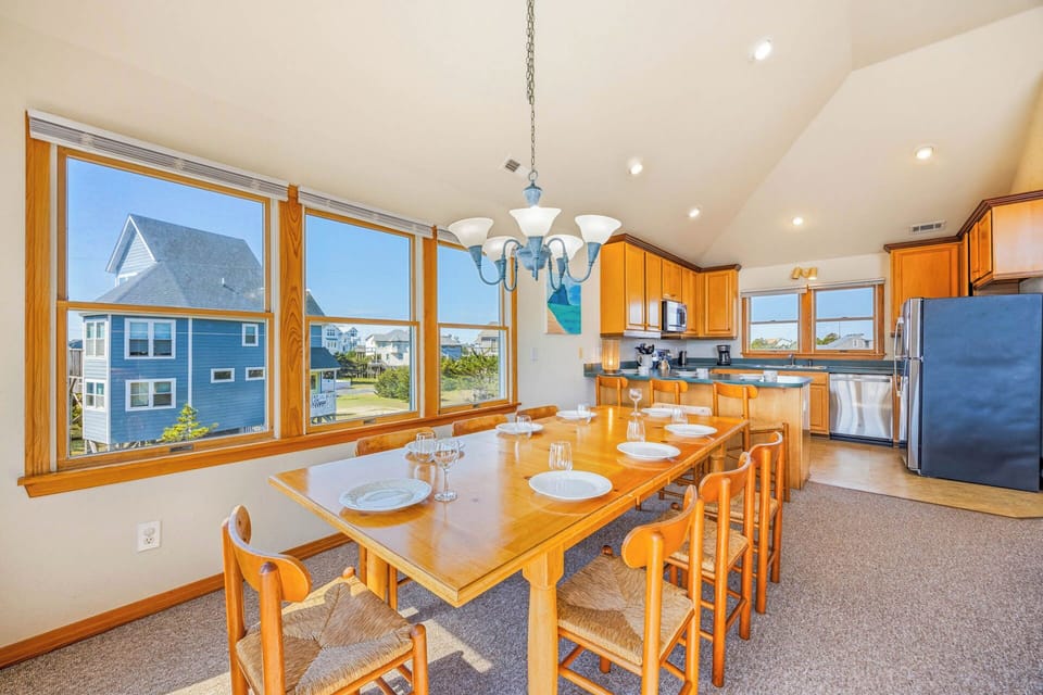 Bright and spacious dining area with vaulted ceilings, large windows flooding the room with natural light, and a welcoming table set for memorable meals together.