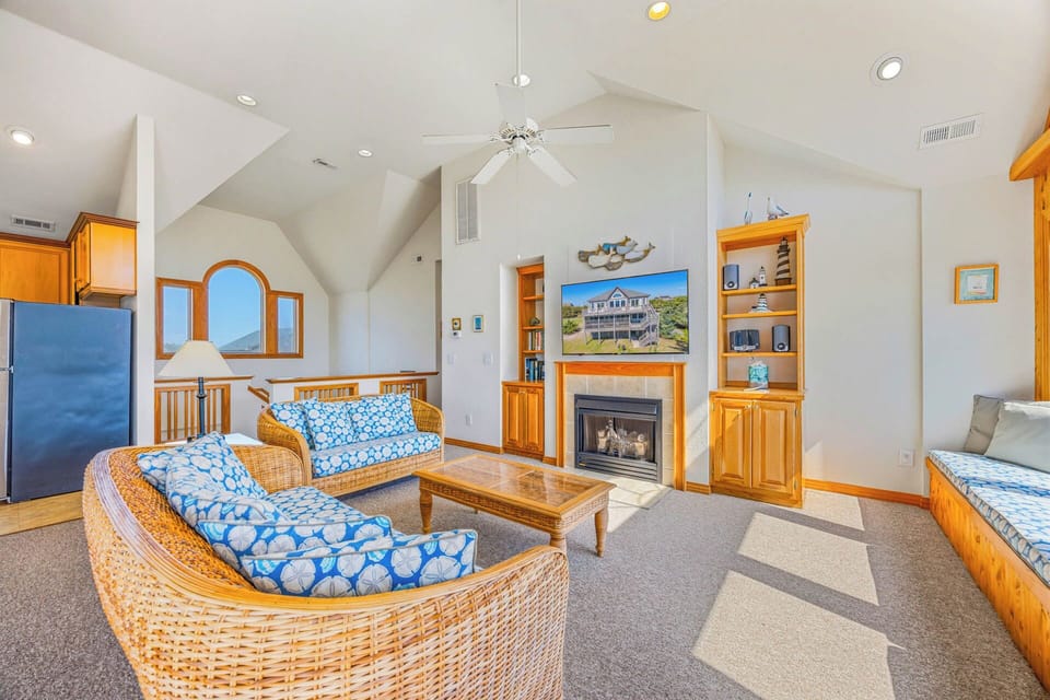 Relax in your spacious living room with soaring vaulted ceilings and coastal charm. Sink into plush wicker seating by the cozy fireplace while natural light pours through arched windows.