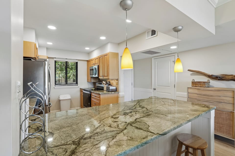 Warm wood tones and gleaming granite countertops create an inviting kitchen, where natural light and golden pendant lights make meal prep a joy.