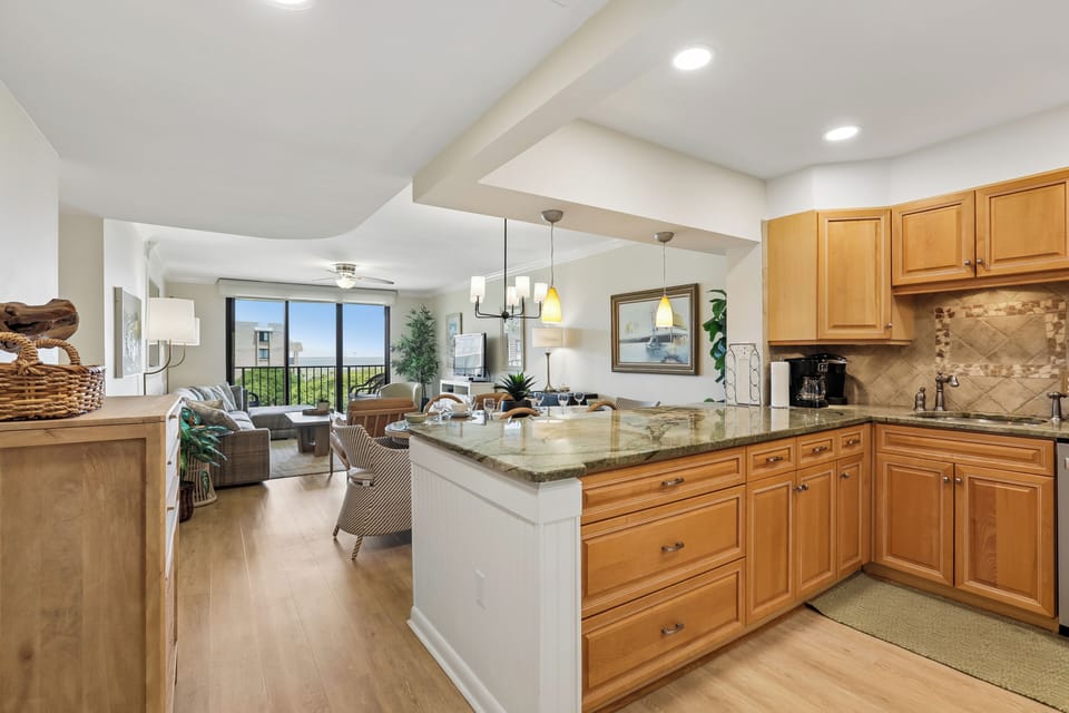 Bright, open living with a sleek kitchen island, warm wood cabinetry, and windows framing green views—your perfect home base for relaxation and connection.