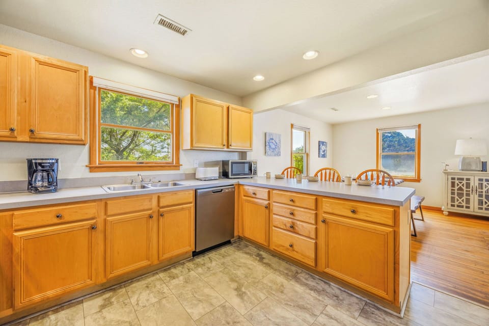 Prepare your favorite meals in this bright, fully equipped kitchen featuring warm wood cabinetry, modern appliances, and lovely views of nature through multiple windows that fill the space with natural light.