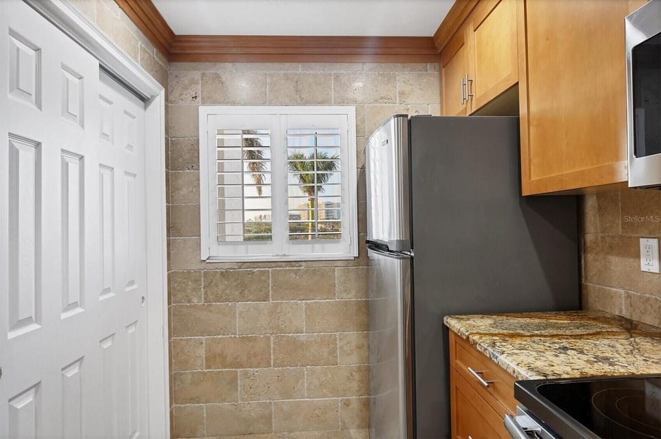 Your fully equipped kitchen features granite countertops, stainless appliances, and warm wood cabinetry with views of swaying palms outside.