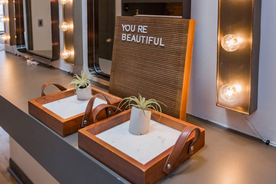 - Cute vanity decor with YOU’RE BEAUTIFUL message included   - Warm lights and wooden trays enhance the glam corner   - Perfect detail for guests getting ready together
