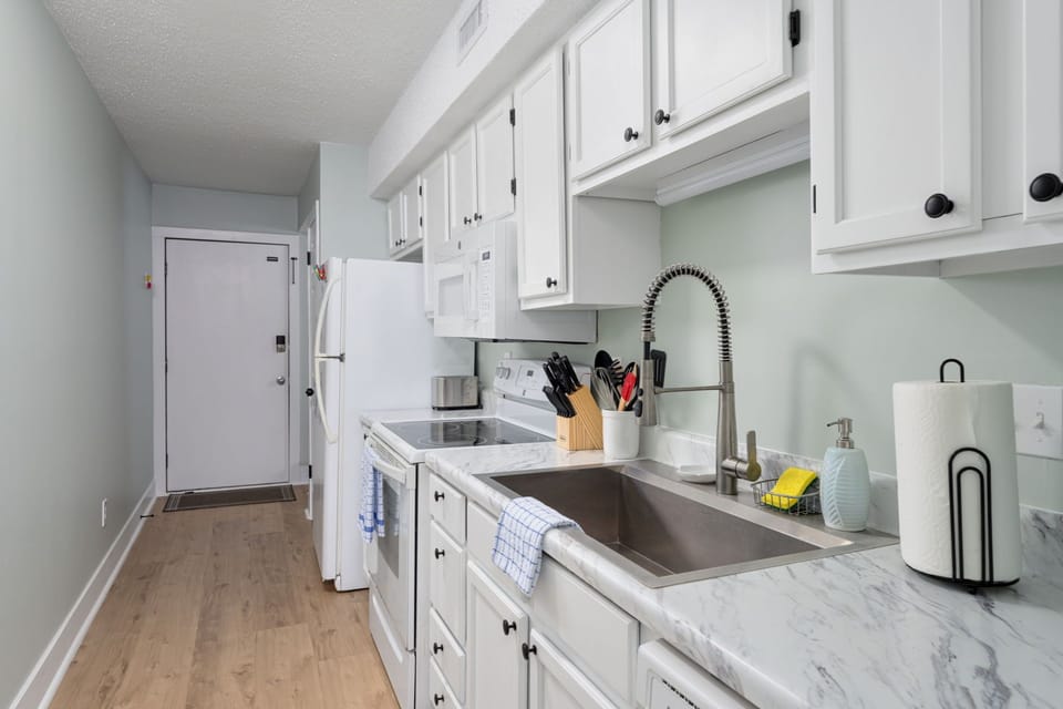 Your fully equipped kitchen features sleek white cabinetry, marble countertops, and modern appliances. Fresh linens and essentials are ready for your use.