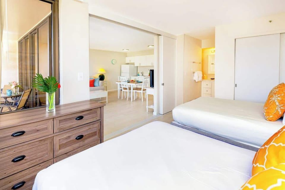 Bright bedroom with two beds and a view into the open kitchen and dining area