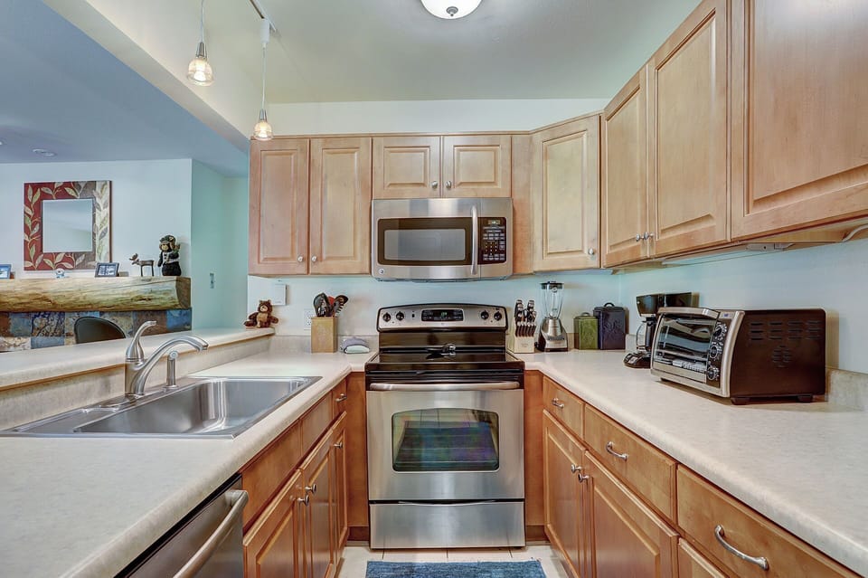 A modern kitchen with stainless steel appliances, light wood cabinets, a double sink, and small appliances like a toaster oven and coffee maker on the countertops.