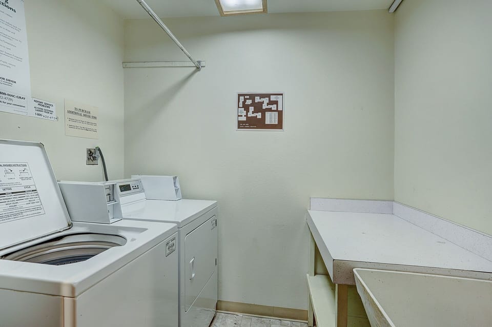 A small laundry room with a washer, dryer, counter space, sink, and wall-mounted instructions and diagram.