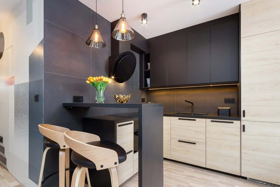 A modern kitchen with black and beige tones, featuring sleek cabinetry and decorative lighting fixtures above the counter.
