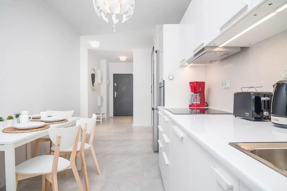 The kitchen with white furniture provides space to cook meals and the table allows you to eat them in a relaxed environment.
