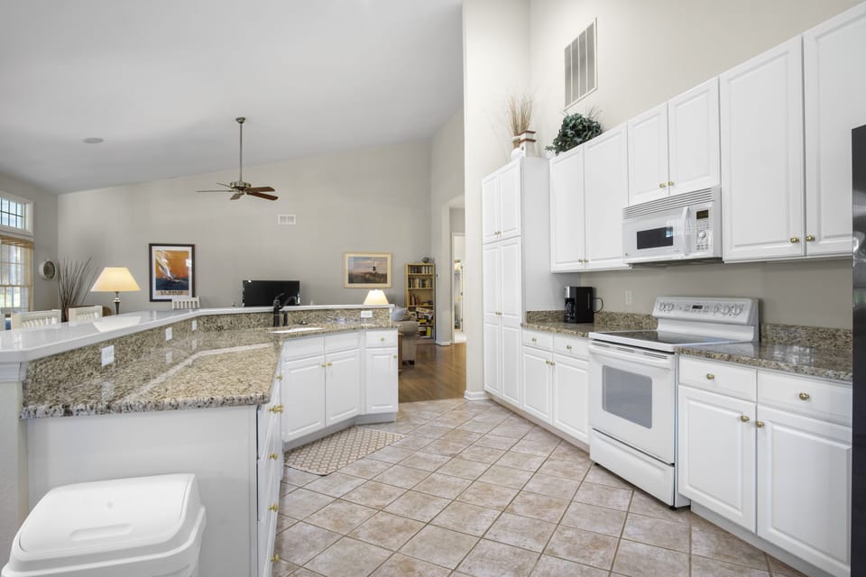 69 Willow Oak Ave - Kitchen Workspace Perspective - This view highlights the seamless transition from the kitchen to the vaulted great room. The space is equipped with modern white appliances, including an electric range and over-the-range microwave, all set against a neutral tiled floor that enhances the airy feel.