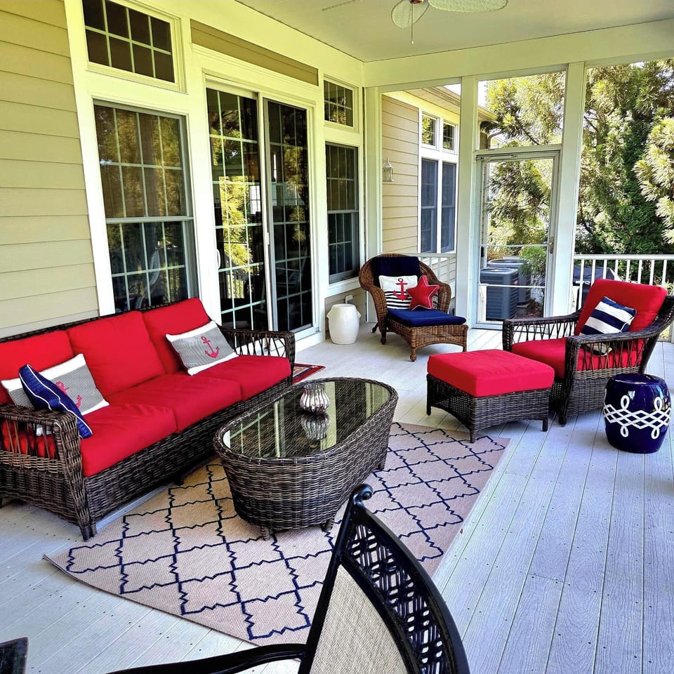 69 Willow Oak Ave - Outdoor Screened Living Space - This spacious screened-in porch offers a comfortable outdoor retreat, furnished with high-quality wicker seating and bold red cushions. A decorative outdoor rug and glass-top coffee table create a full living room experience while enjoying the fresh air and views of the surrounding greenery.