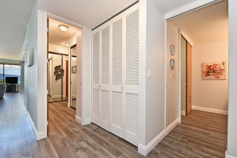 Hallway with wood‑style flooring, louvered closet doors, and decorative wall art leading into other rooms.